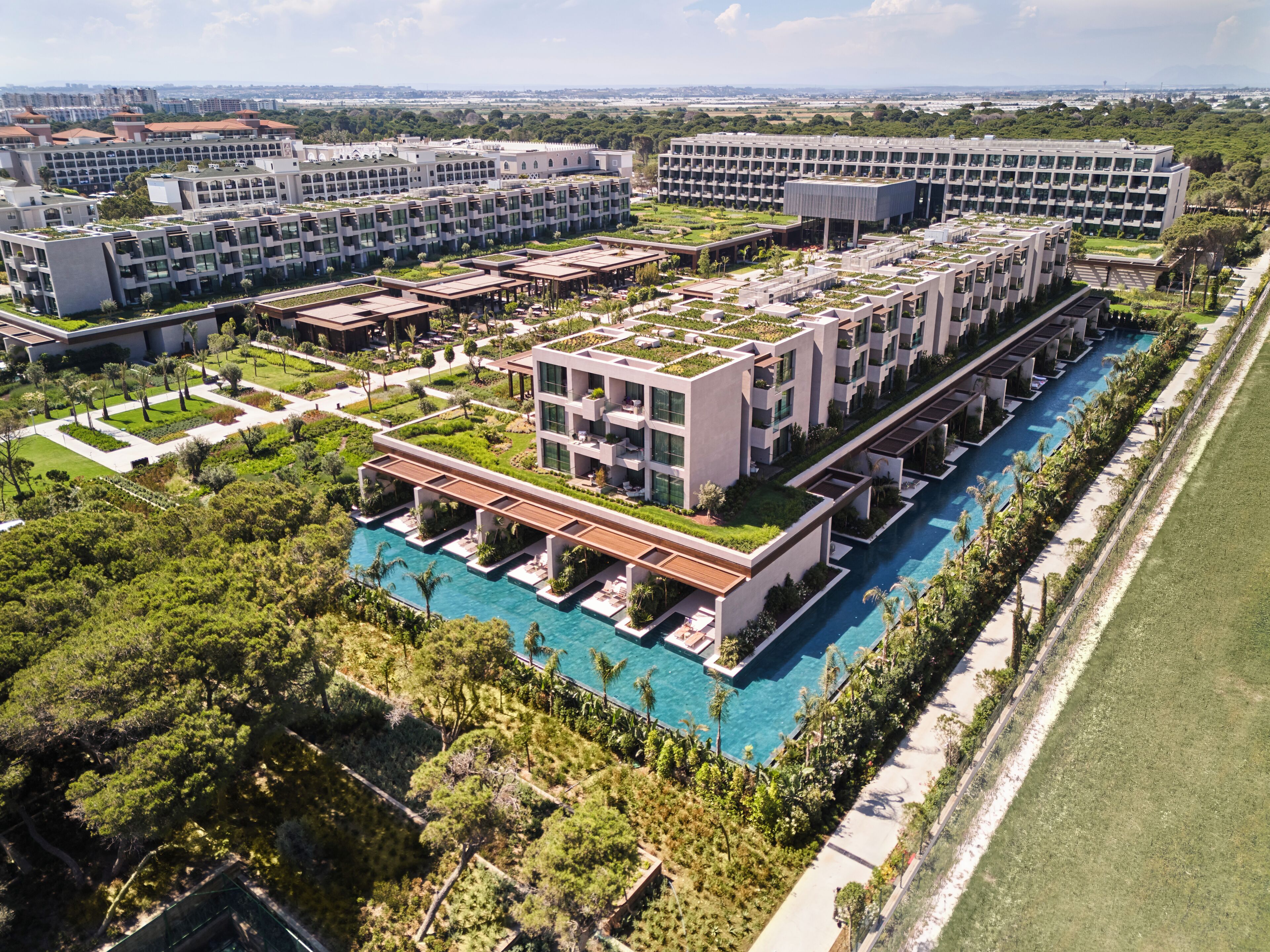 A modern hotel complex with multiple buildings, rooftop gardens, and a central swimming pool.