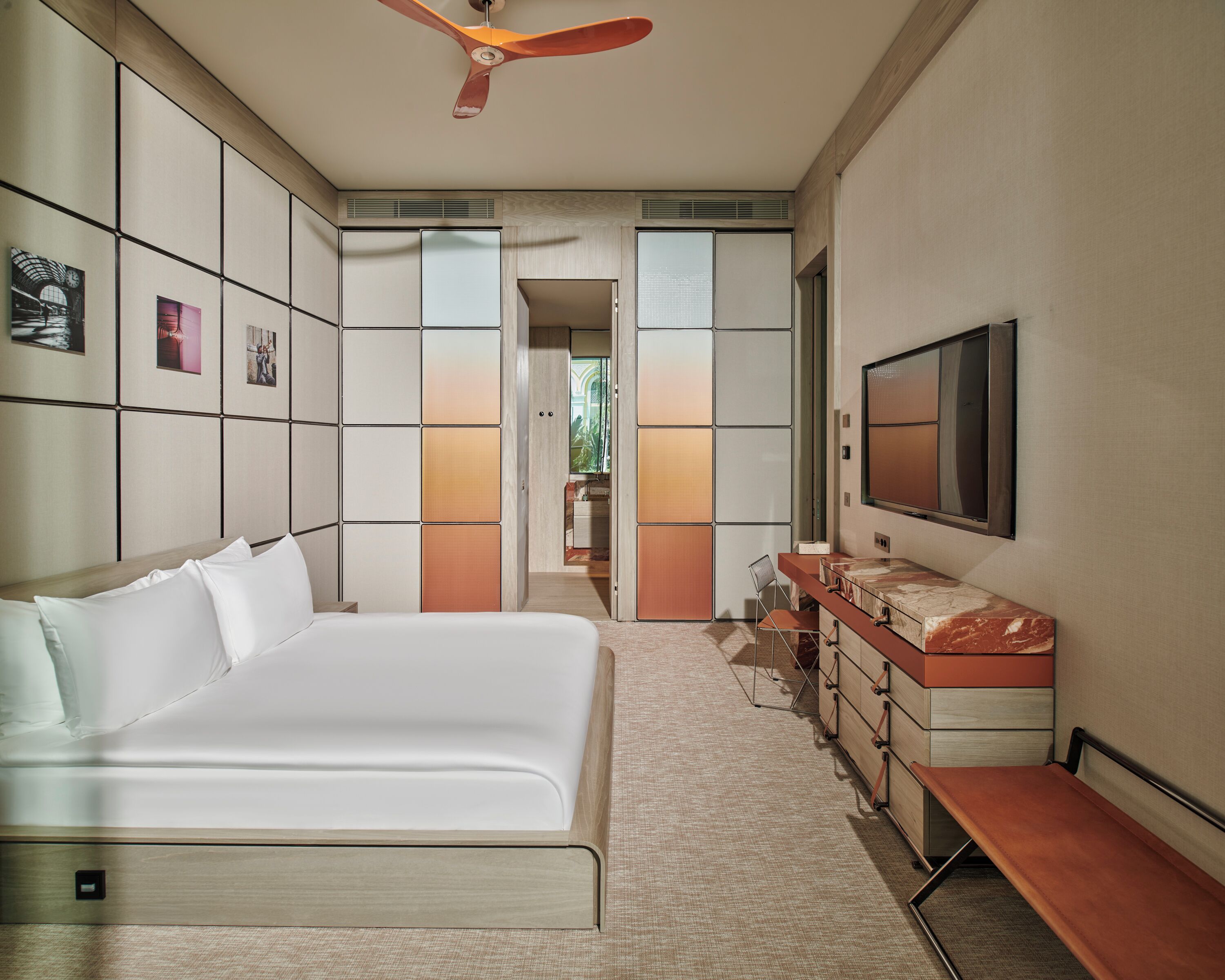 Ein Hotelzimmer mit einem Bett, einem Schminktisch mit Spiegel, einem Fernseher und einem Deckenventilator.