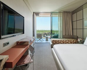A hotel room with a bed, a TV, a desk, a chair, and a view of the outdoors. - Voyage Kundu (Antalya)