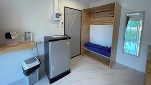 Une petite cuisine équipée comprenant un réfrigérateur, une petite poubelle, une étagère en bois avec des bouteilles et une fenêtre donnant sur un paysage verdoyant.