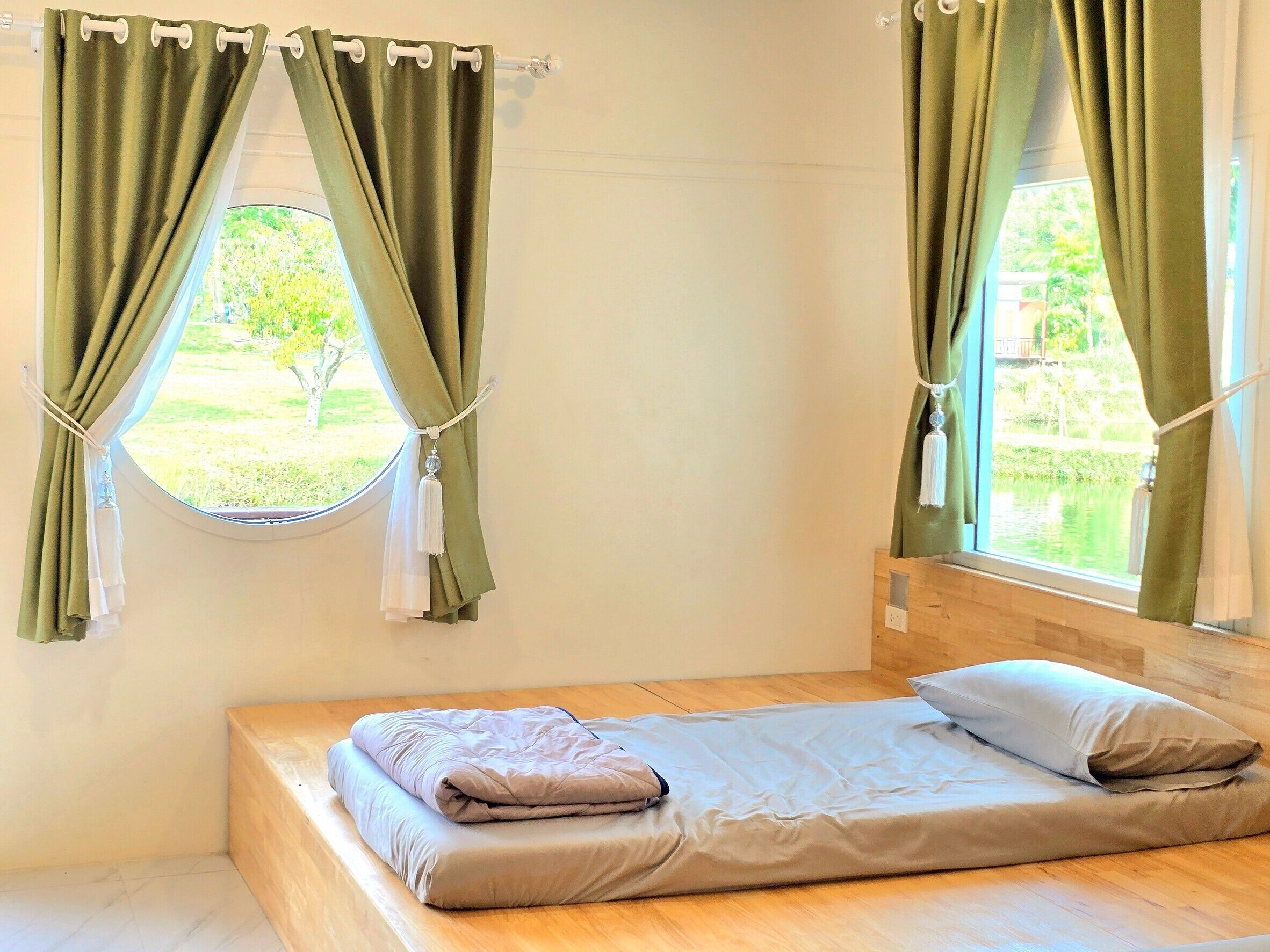 A single bed with a wooden headboard in a room with two windows, each with green curtains tied back.