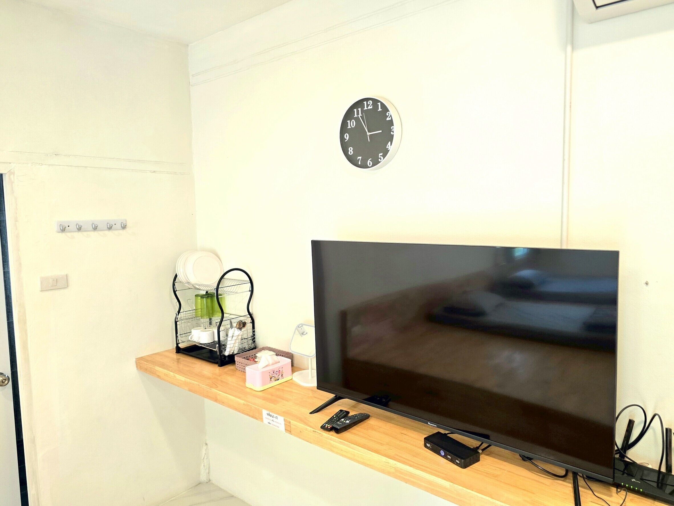 A room with a wooden counter, a flat-screen TV, a clock, and a power strip.