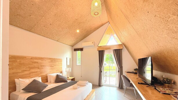 Une chambre avec un plafond en bois, un lit avec des oreillers, un bureau avec une télévision et une fenêtre avec des rideaux.