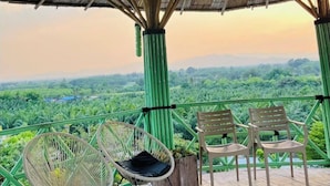 Une terrasse en bois avec deux fauteuils en osier et une table en bois, offrant une vue sur un paysage verdoyant et luxuriant.