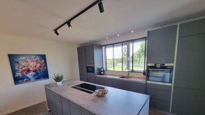 Una cocina moderna con una isla central, armarios grises y un ventanal con vistas a zonas verdes.