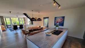 Una cocina moderna con una isla central, una zona de comedor con mesa de madera y un ventanal con persianas.