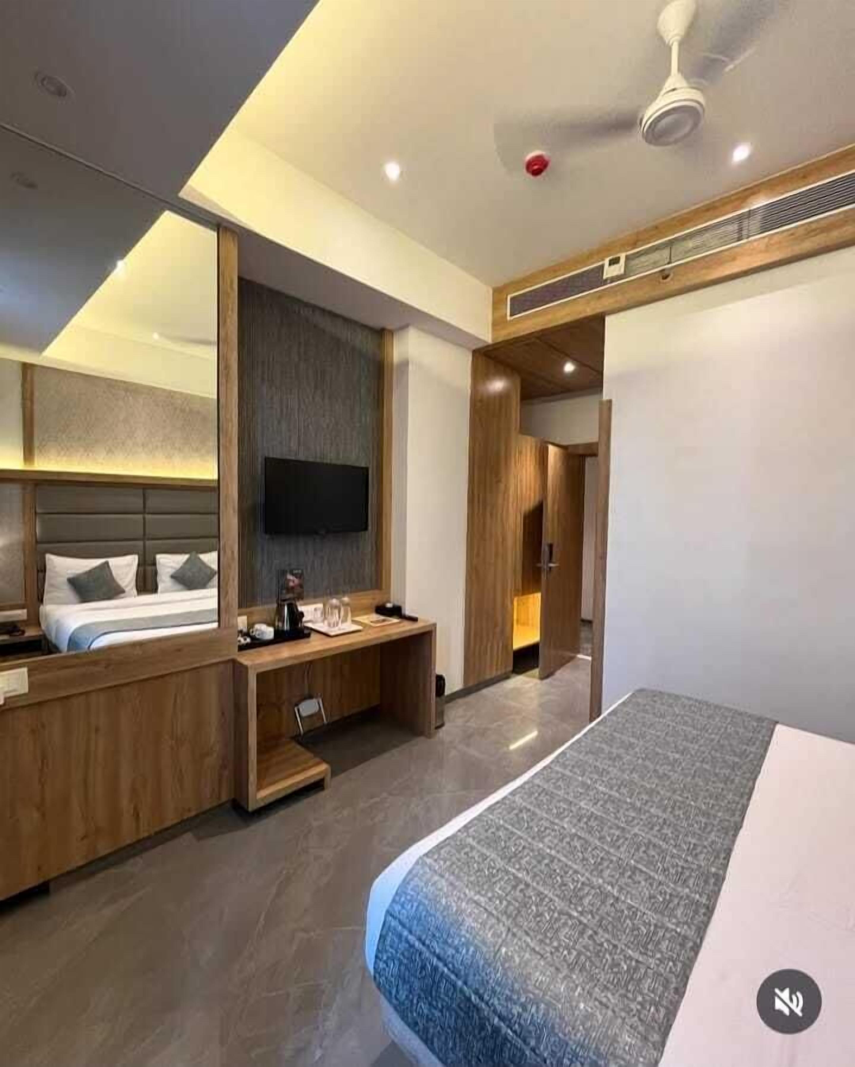 A modern hotel room with a large bed, a desk, a flat-screen TV, and a ceiling fan.