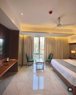 A hotel room with a bed, a TV, a desk, two chairs, a table, and a ceiling fan.