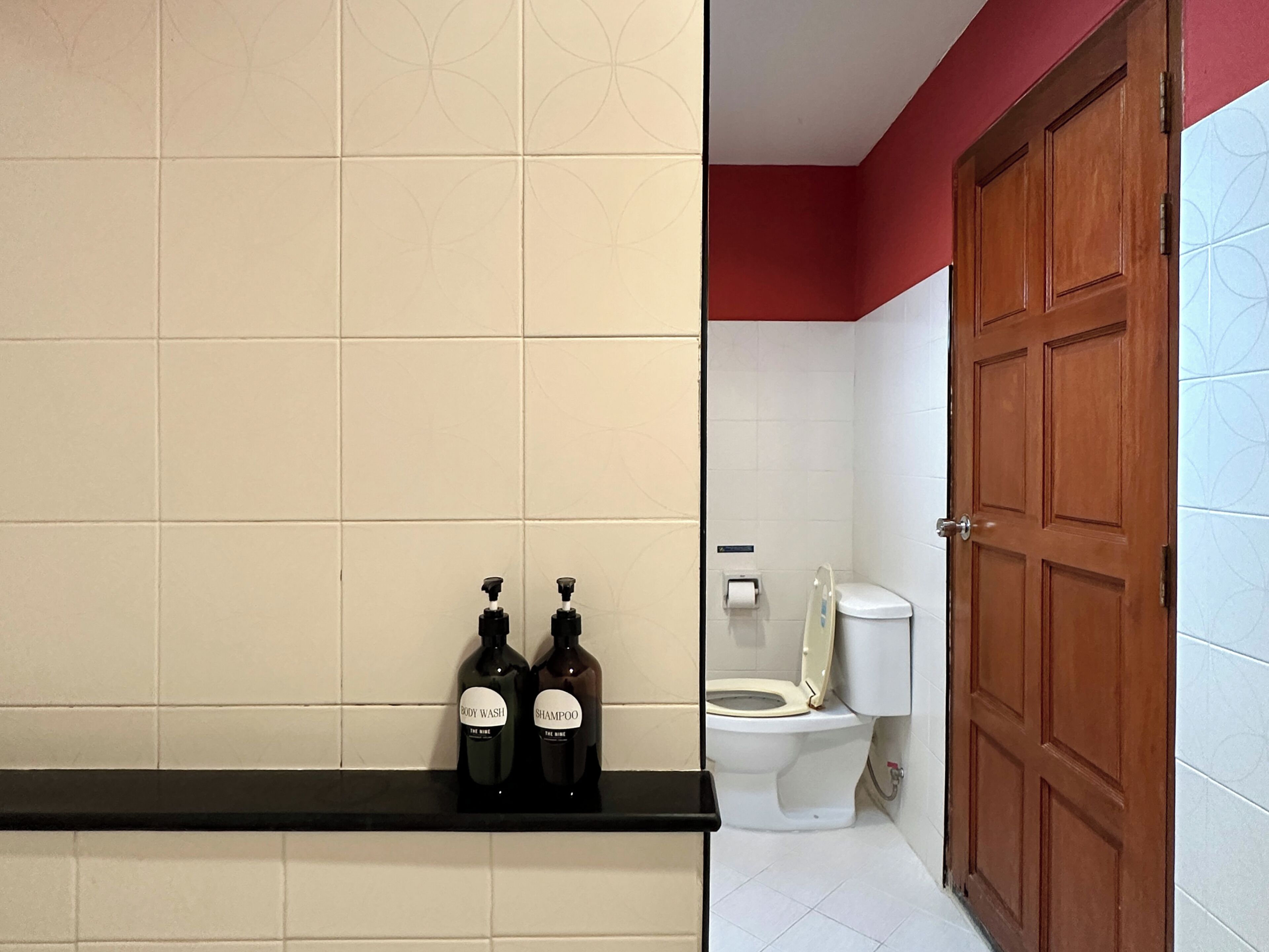 A bathroom with a toilet, a shelf with two bottles, and a wooden door.