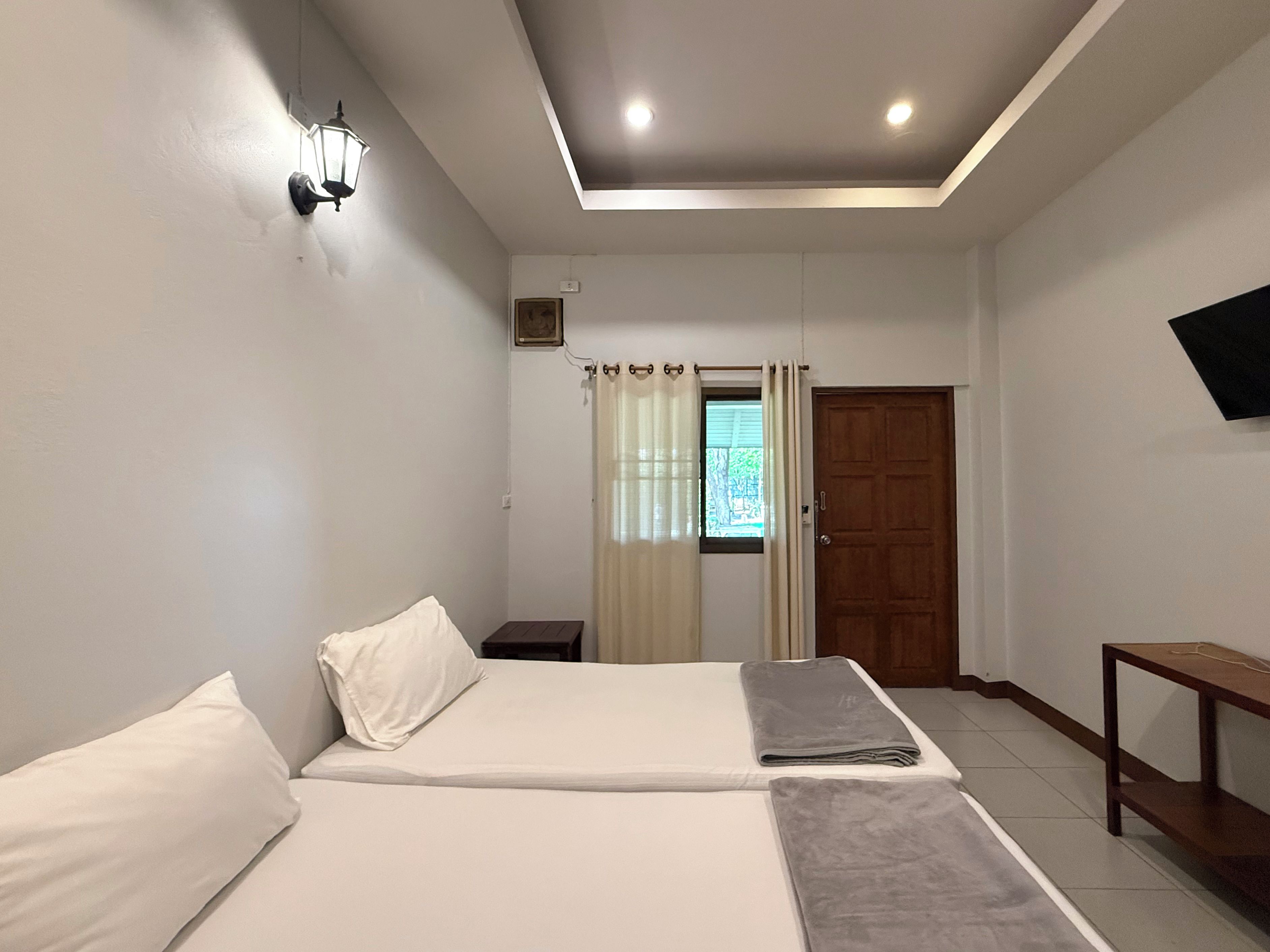 A hotel room with two beds, a wooden door, a TV mounted on the wall, and a small table.