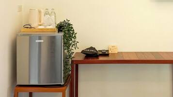 A compact kitchenette with a stainless steel refrigerator, a small wooden table, and a potted plant.