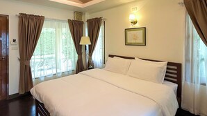 Habitación de hotel con una cama grande, una mesita de noche con lámpara, un cuadro en la pared y cortinas en las ventanas.