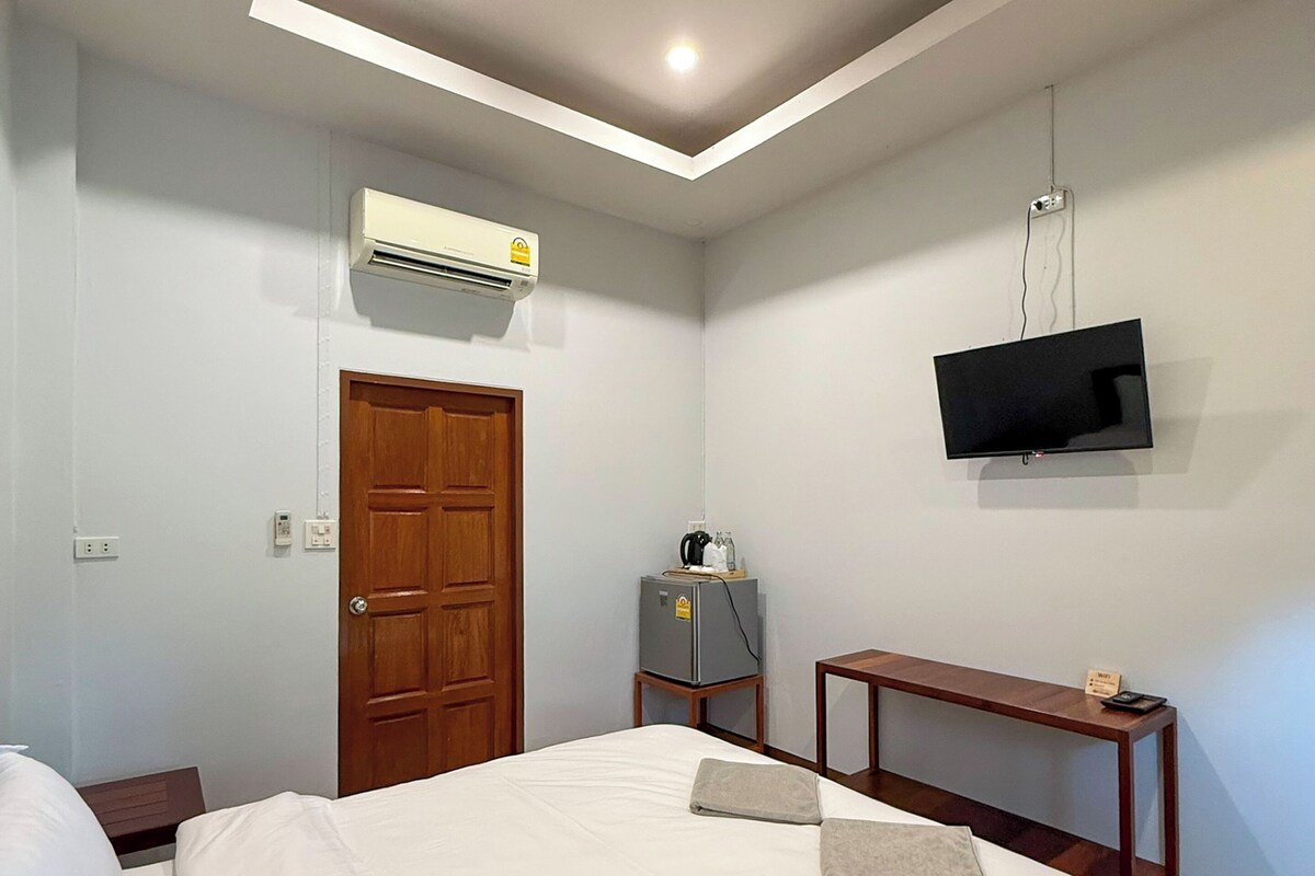 Une chambre d’hôtel avec un lit, un téléviseur fixé au mur, un climatiseur et une petite table.