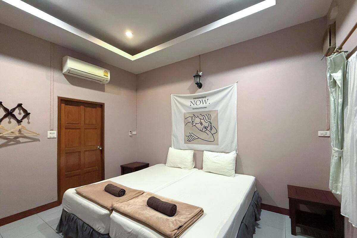 A bedroom with a bed, a wooden door, an air conditioning unit, a wall-mounted light fixture, and a banner with text.