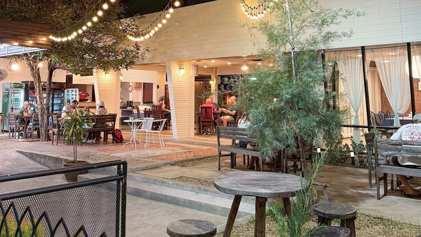 Un espacio de comedor al aire libre con luces colgantes, mesas y sillas.