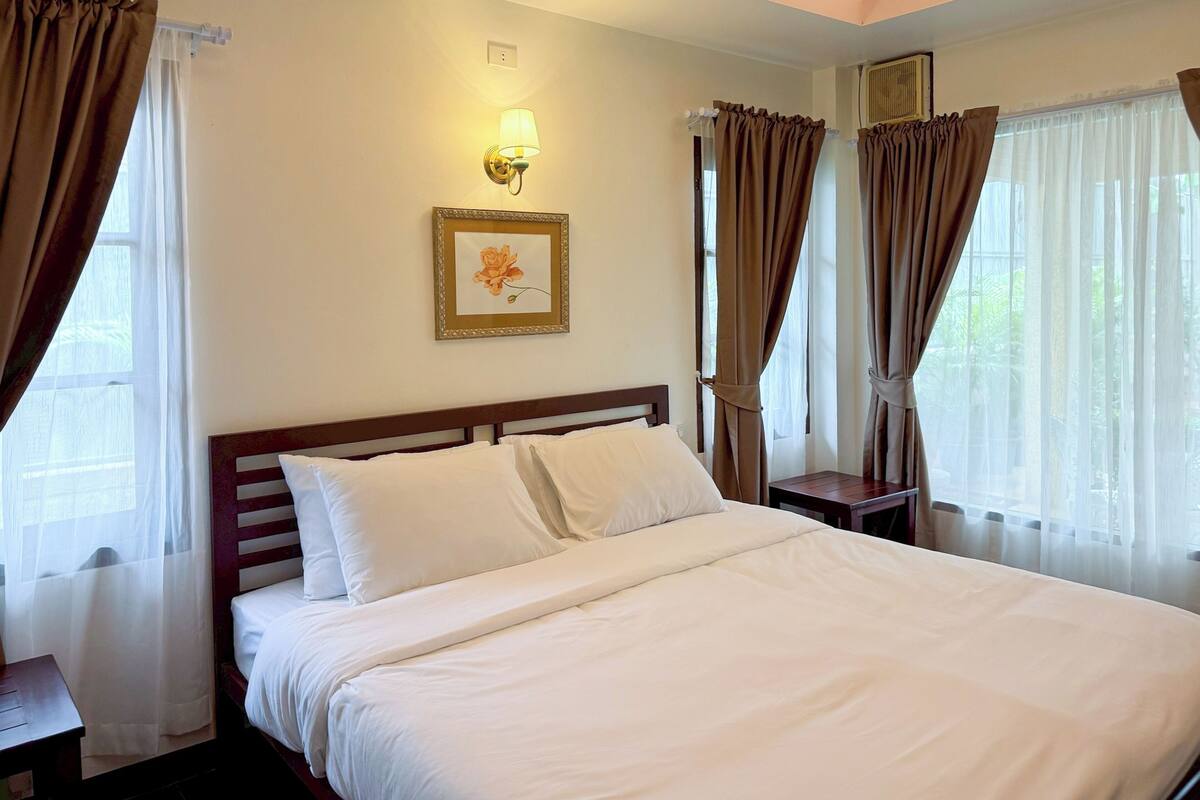 A hotel room with a neatly made bed, a bedside table, a lamp, and a framed picture on the wall.