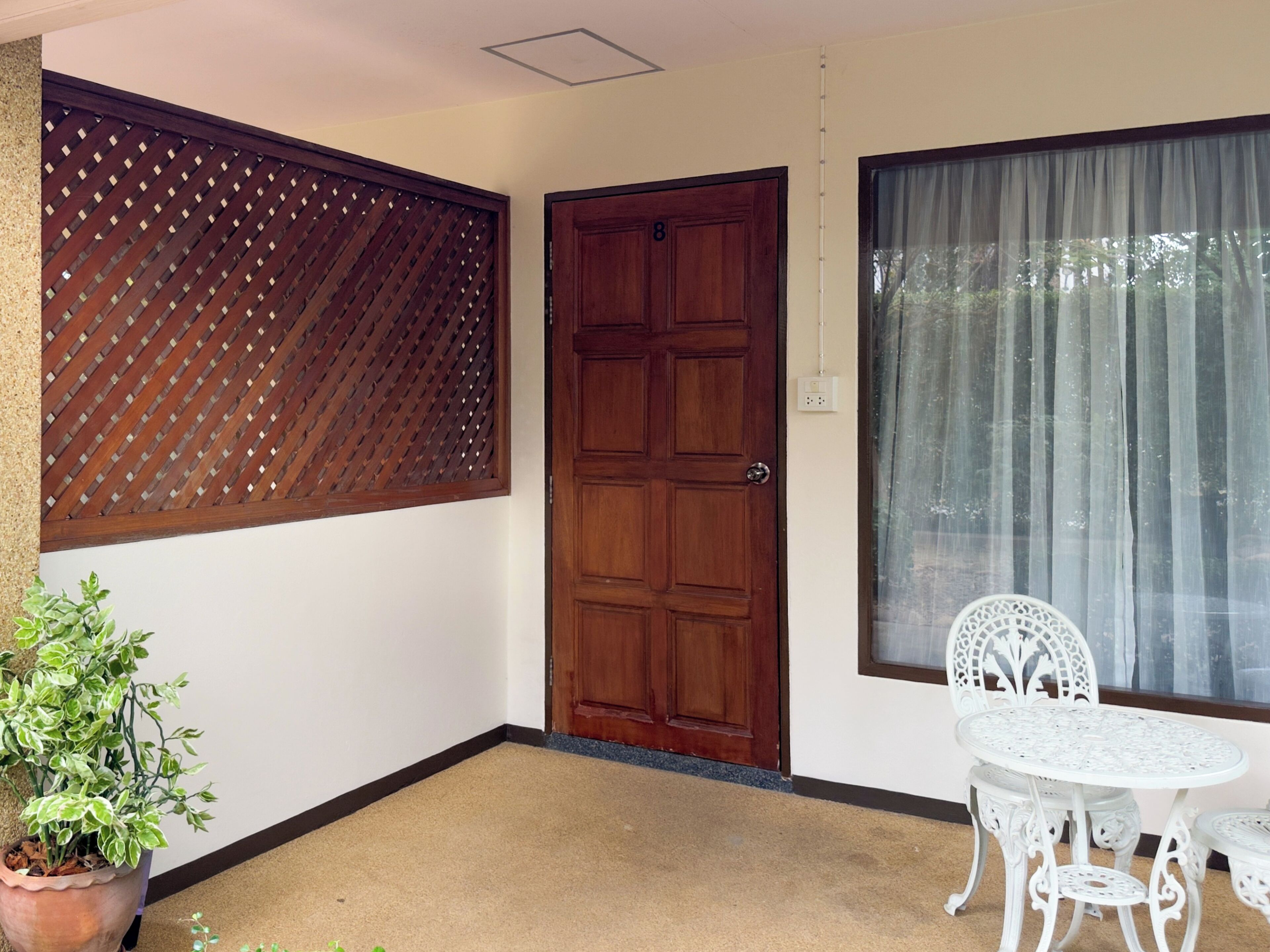 A room with a wooden door, a window with sheer curtains, a potted plant, and a white table with chairs.