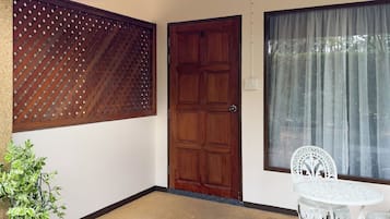 A room with a wooden door, a window with sheer curtains, a potted plant, and a white table with chairs.
