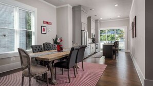 Un coin repas avec une table en bois, des chaises à revêtement gris et un tapis aux motifs rouges et blancs.