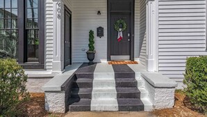 Une maison avec un porche à l’avant, un escalier à rayures noires et blanches, une guirlande sur la porte et une plante en pot.