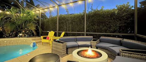 An outdoor patio with a pool, lounge seating, and a fire pit.