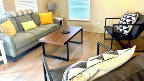 A living room with a grey sofa, yellow cushions, a wooden coffee table, and a black and white patterned armchair. - Minutes away from the beach and walking distance into town (St. Augustine)