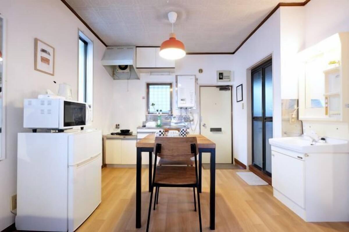 A compact kitchen with a dining table and chairs, a microwave, a refrigerator, and a sink.