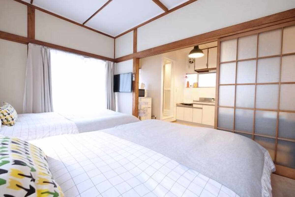 A hotel room with two beds, a sliding shoji screen, a TV, and a kitchenette.