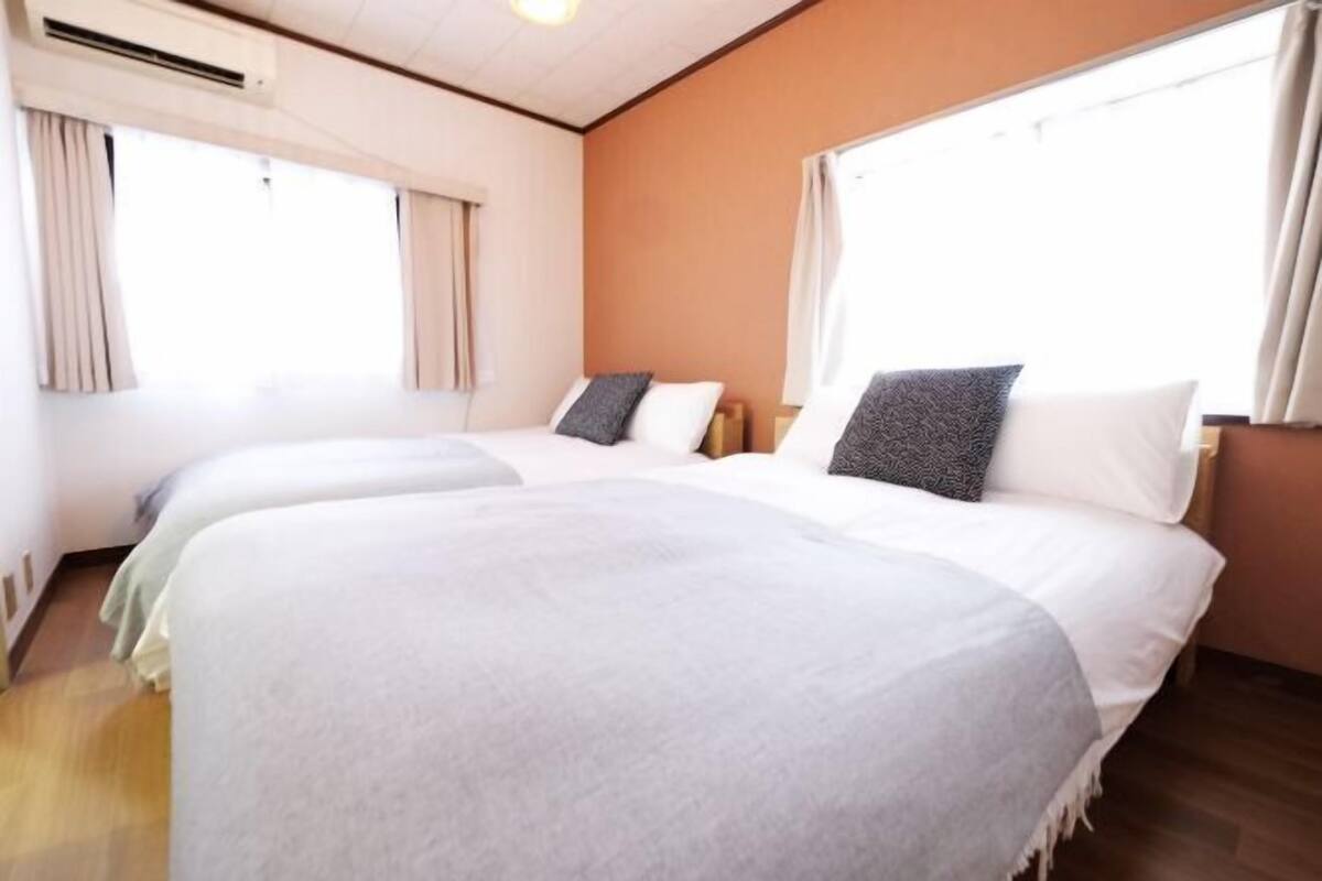 A hotel room with two beds, a window, and an air conditioning unit.