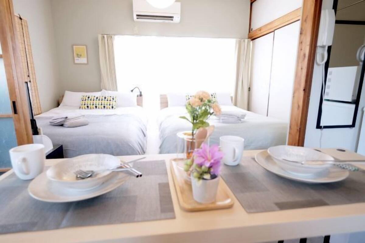 A hotel room with two beds, a dining table with plates and utensils, and a small table with a flower vase.