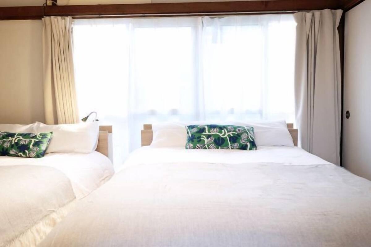 A hotel room with two beds, a window with curtains, and a view of the outside.