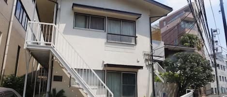 A two-story residential building with a balcony, a staircase, and a small garden area with potted plants.