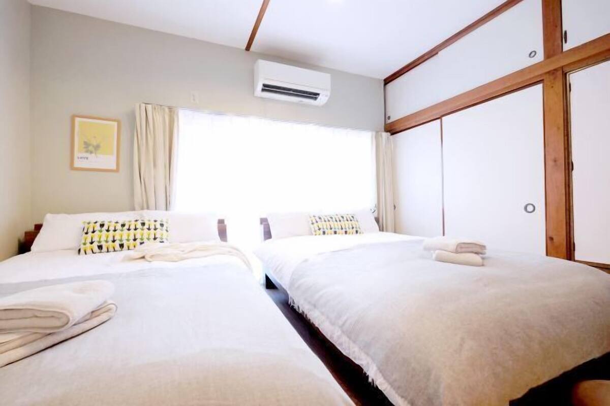 A hotel room with two beds, a window with curtains, an air conditioning unit, and a wooden wardrobe.