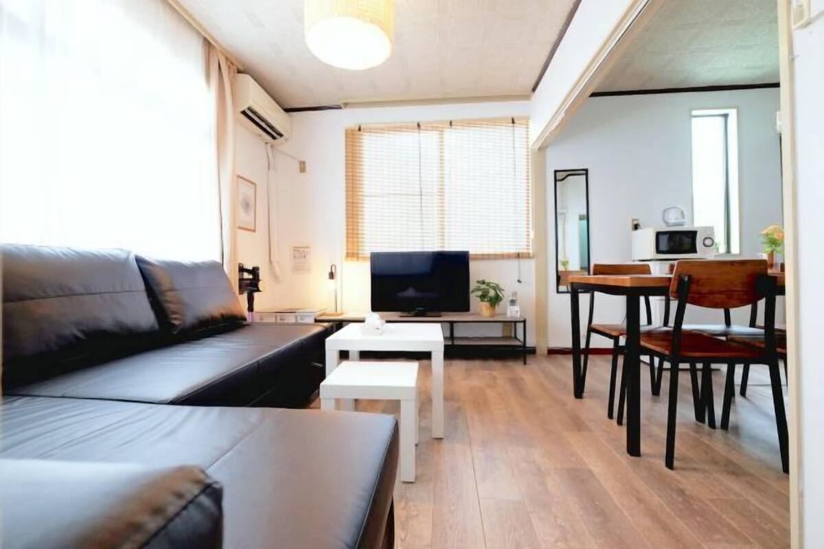 A modern living room with a sofa, a TV, a dining table with chairs, and a kitchen area with a microwave.