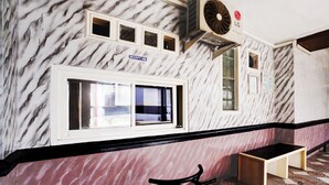 A reception area with marble walls, a reception desk, a bench, and a fan. - Hotel O Omah Bratan (Malang)