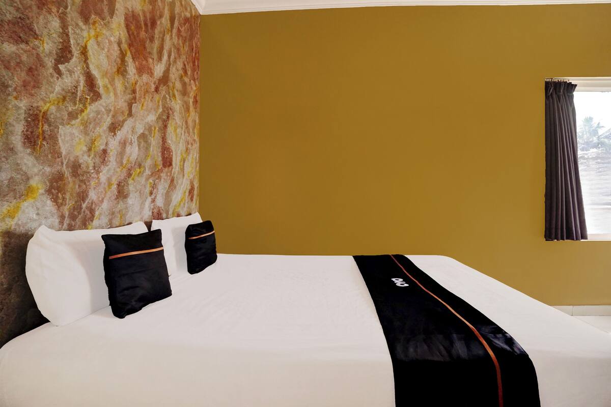 Ein Hotelzimmer mit einem großen Bett, einer Marmorwand, einem Fenster mit Vorhängen und Blick aufs Meer.