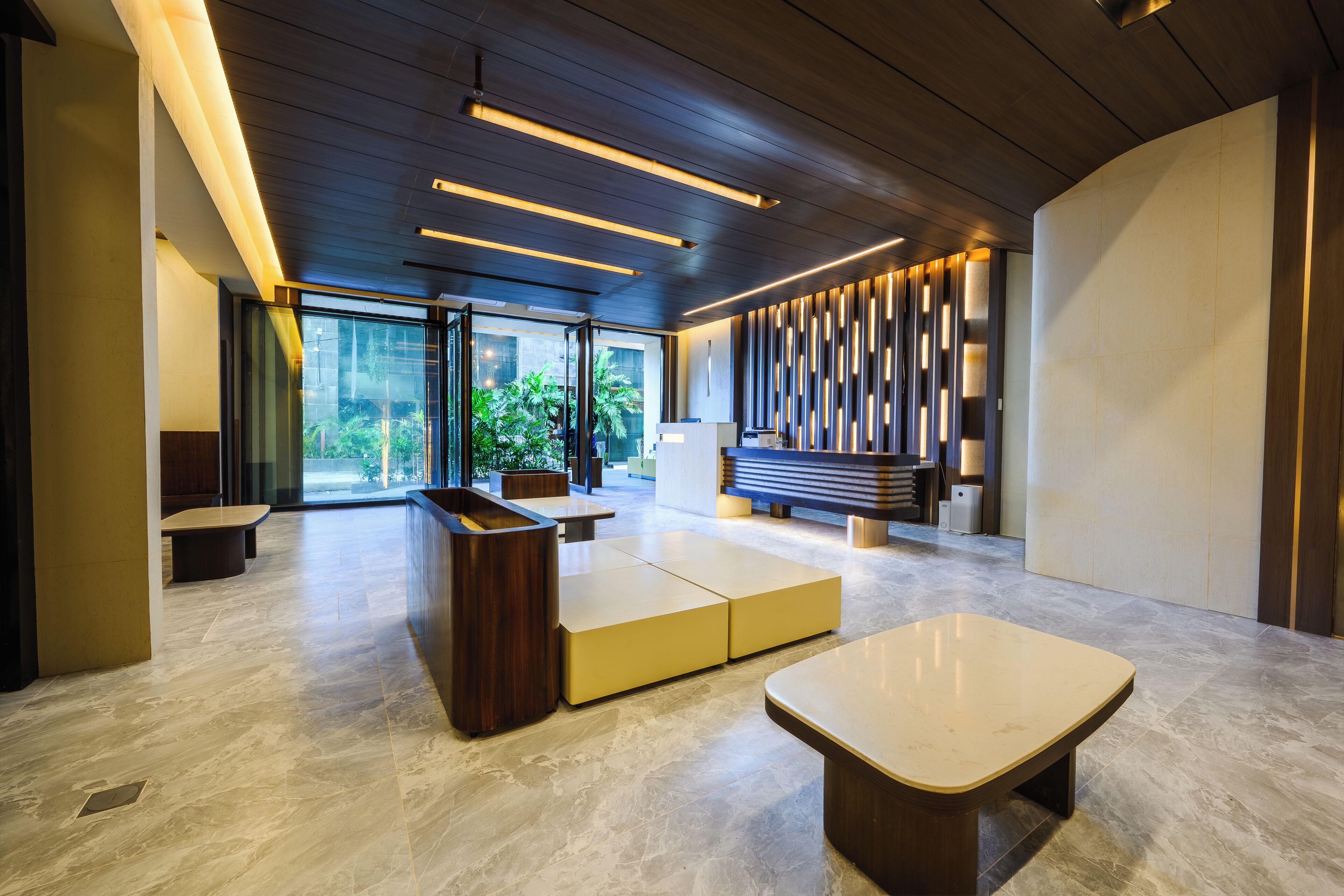 A modern lobby with a reception desk, seating areas, and a large window offering a view of greenery.
