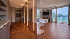 A modern hotel room with a wooden floor, a bed, a TV, and a balcony with a view of the sea.