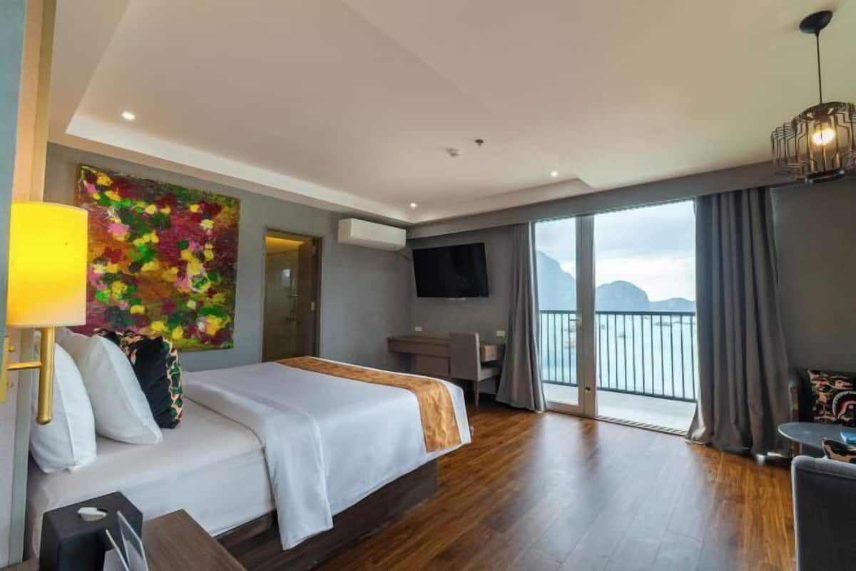 A hotel room with a bed, desk, chair, TV, and a balcony with a view.