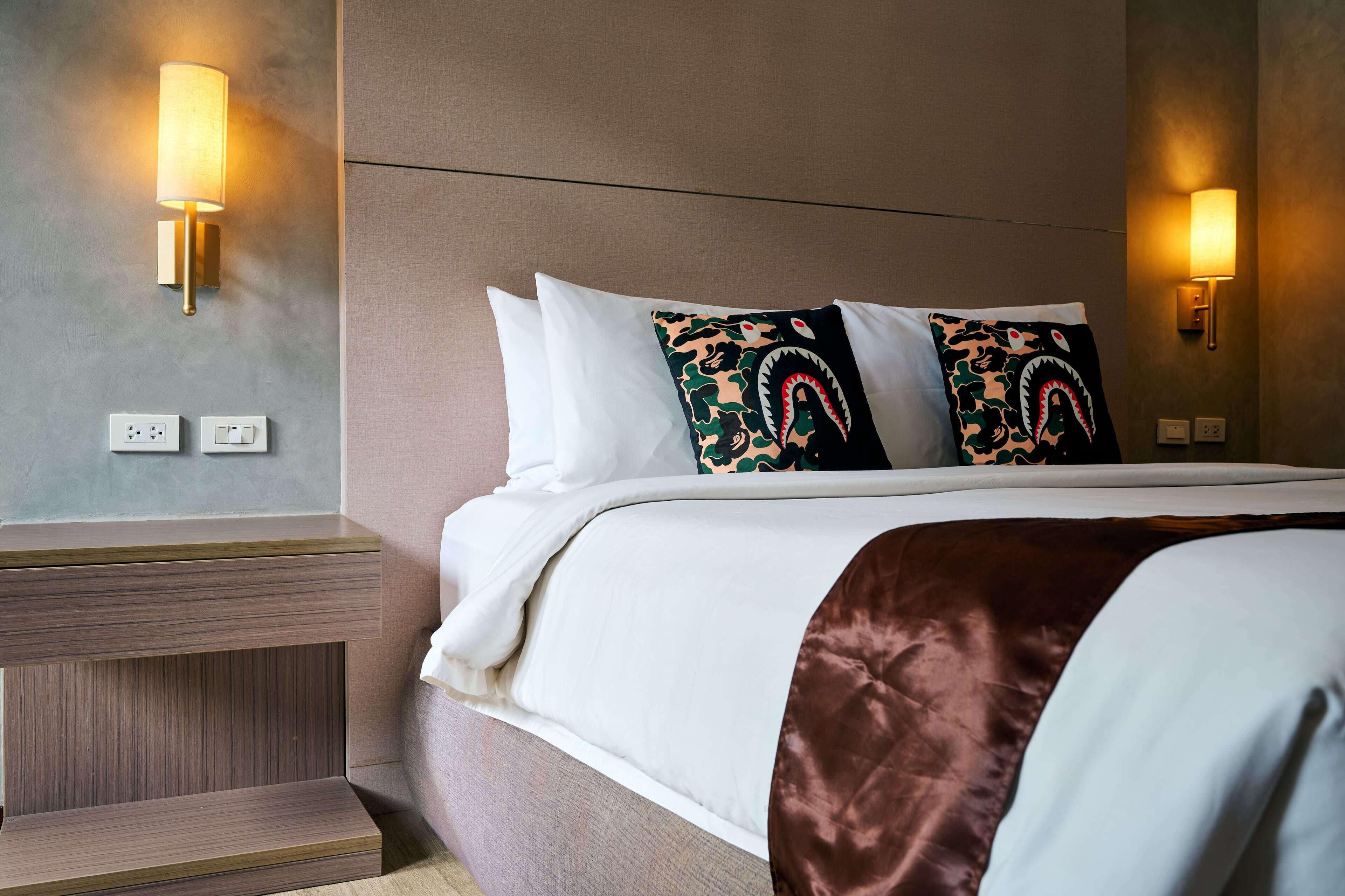Une chambre d’hôtel équipée d’un lit, de deux lampes fixées au mur, d’une table de chevet et d’une prise de courant.