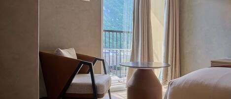 A hotel room with a bed, a chair, a small table, and a balcony with a view of a mountain.