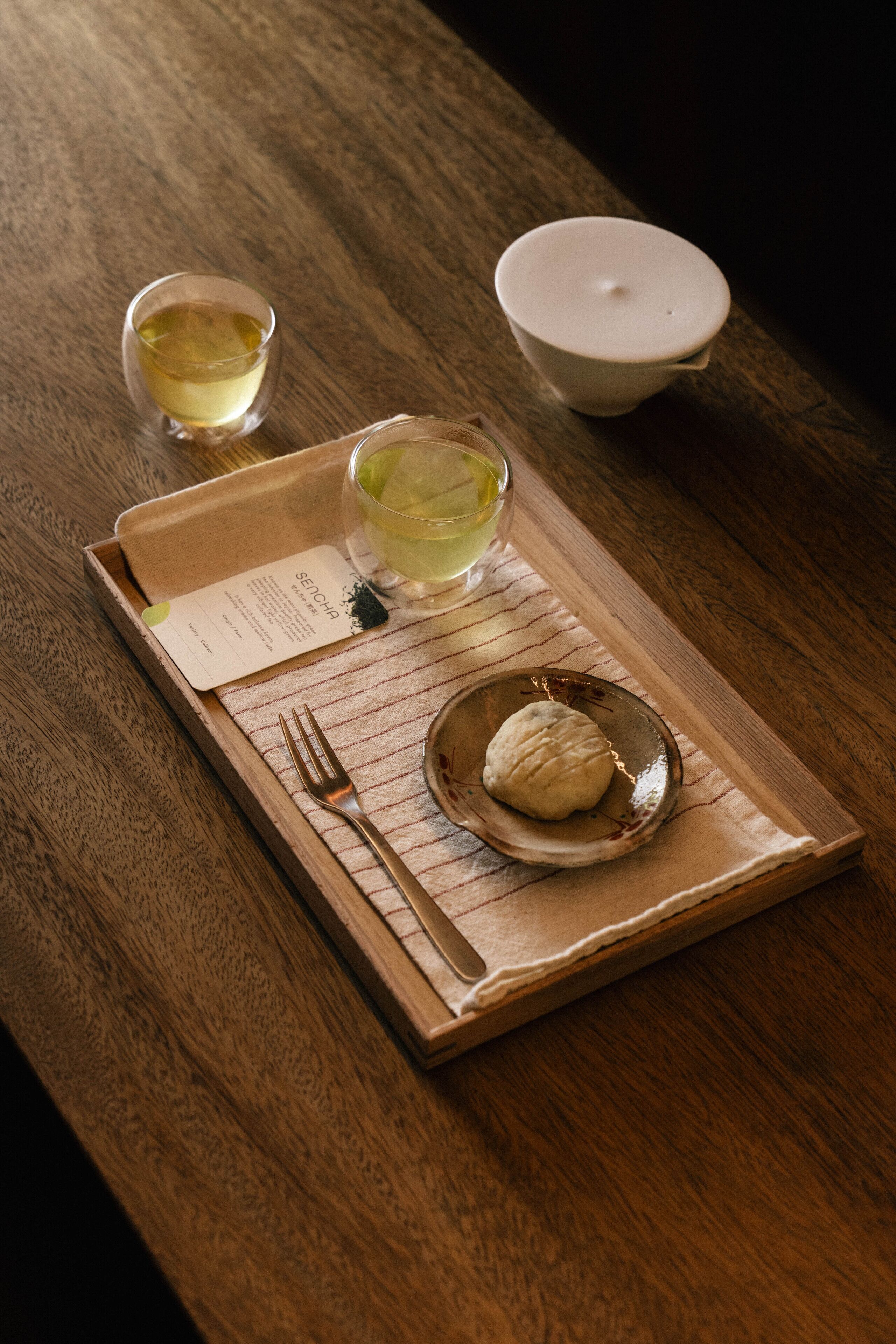 Una bandeja de madera con un menú, una taza de té, un bol de dumplings y una tetera.