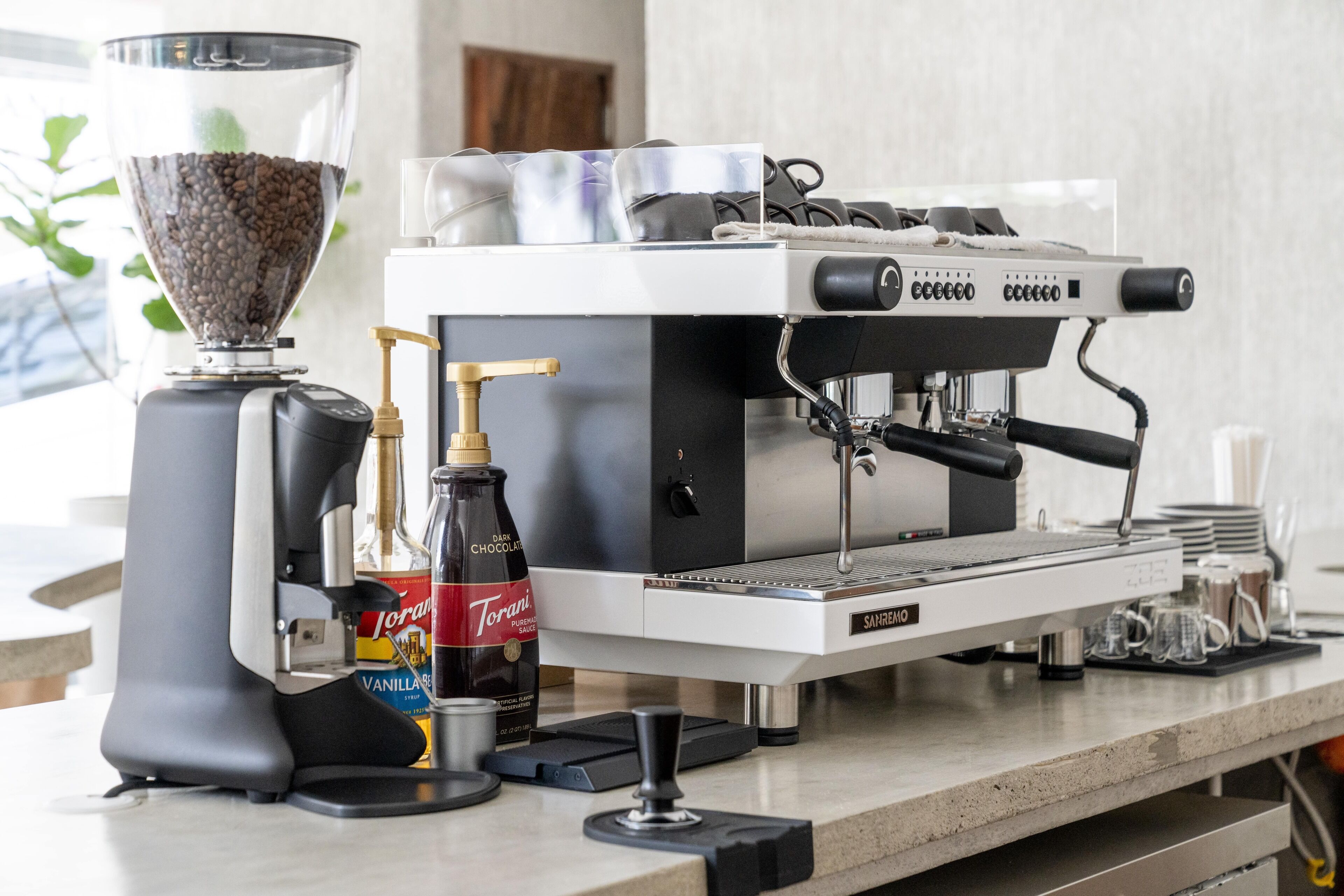Una máquina de café con un molinillo, una botella de sirope Torani y una botella de sirope de vainilla.