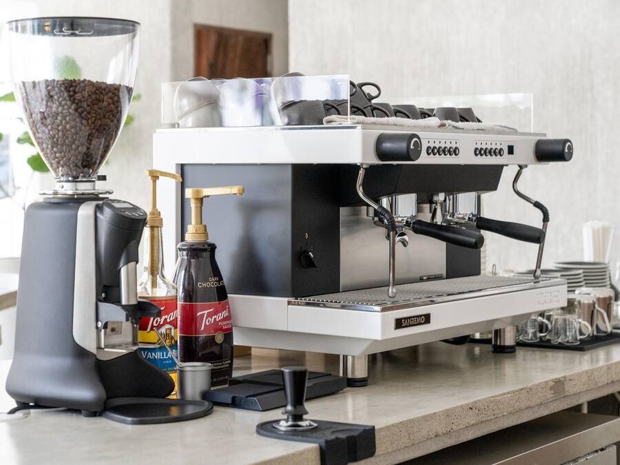 Una máquina de café con un molinillo, una botella de sirope Torani y una botella de sirope de vainilla.