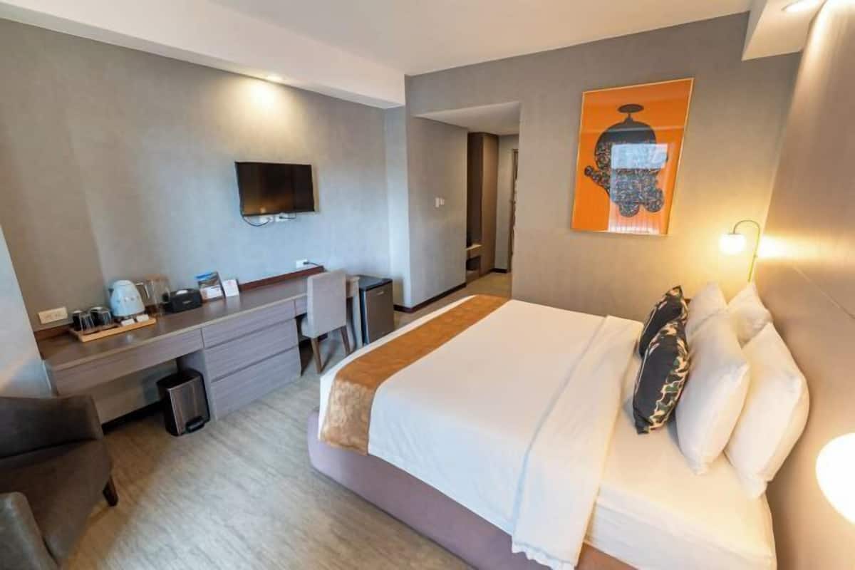 A hotel room with a bed, a desk, a chair, a TV, and a painting on the wall.