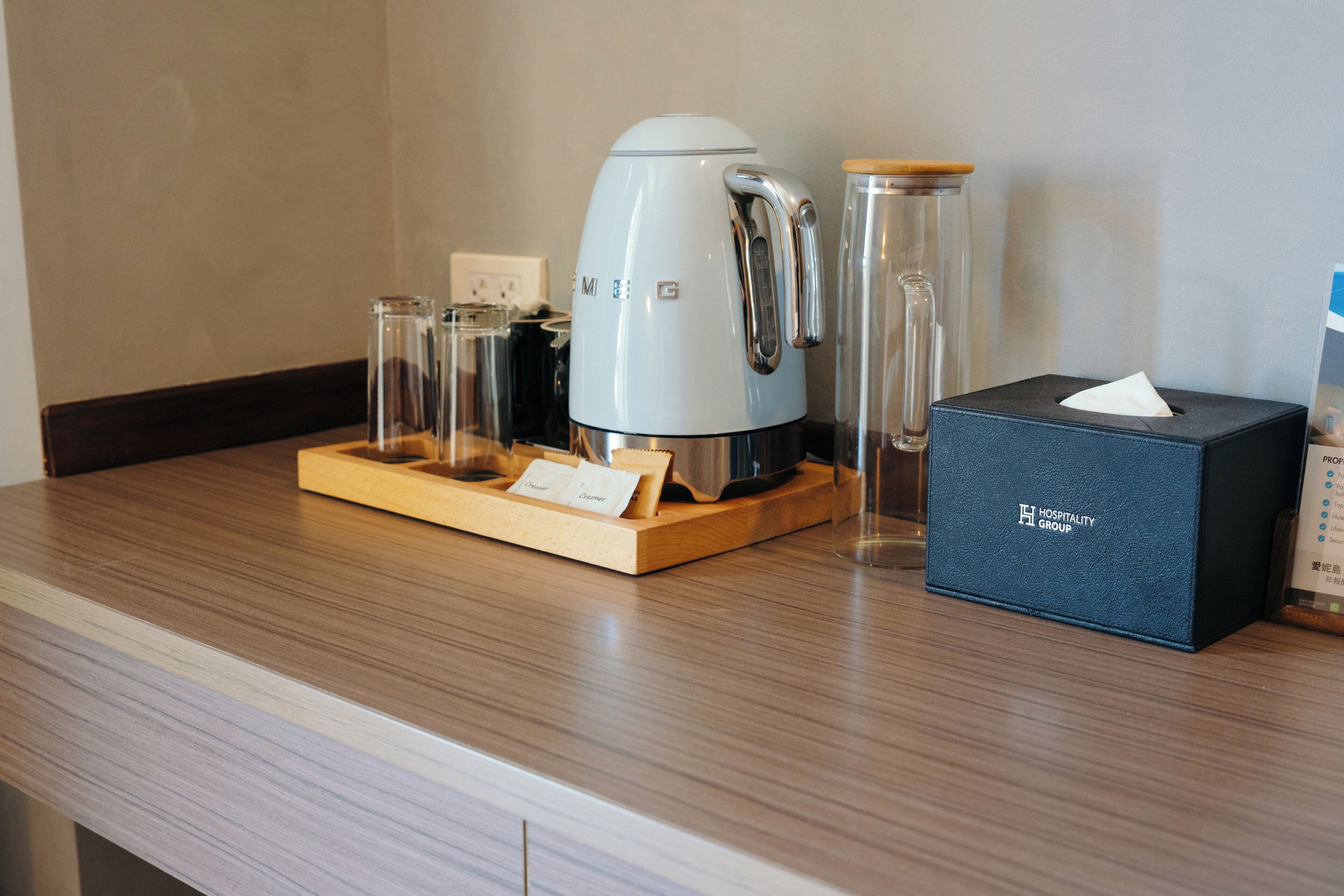 A hotel room's kitchenette with a coffee maker, a glass container, a tissue box, and a wooden tray.