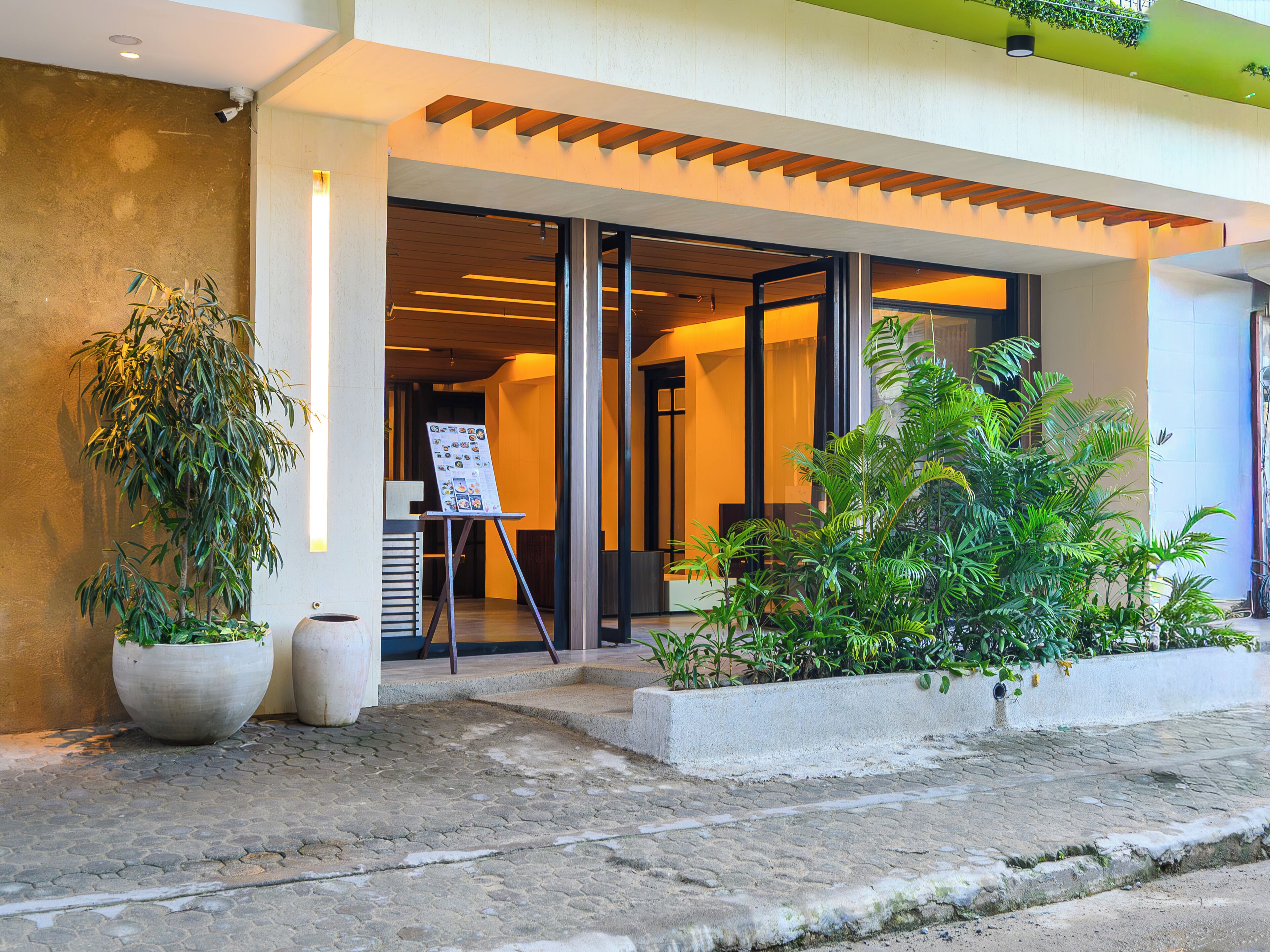 A building entrance with a wooden overhang, potted plants, and a display board.