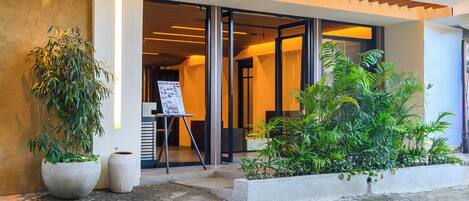 A building entrance with a wooden overhang, potted plants, and a display board.