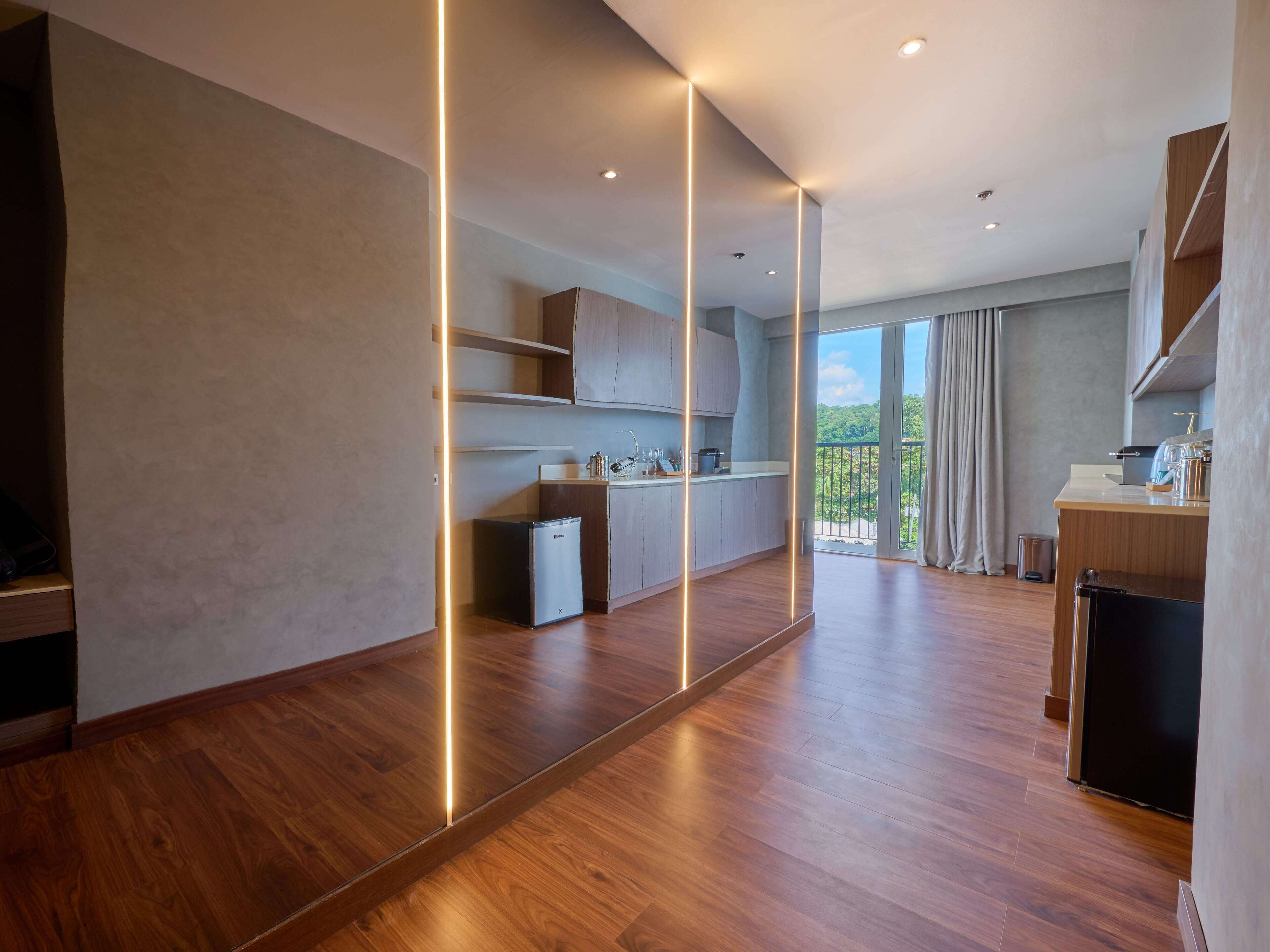 A modern kitchen with wooden flooring, built-in cabinets, and a view of greenery through the balcony.