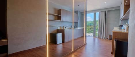 A modern kitchen with wooden flooring, built-in cabinets, and a view of greenery through the balcony.